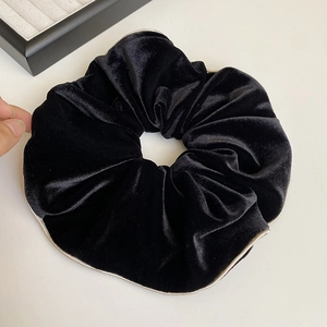 Détail d'un grand chouchou en velours noir avec bordure dorée élégante et texture douce