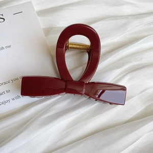 Macro detail of glossy dark red bow-shaped hair claw clip on soft white fabric background
