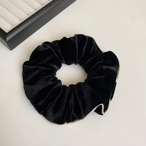 Détail du chouchou en velours noir avec bordure dorée et texture plissée élégante