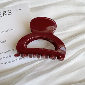 Detail of a large wine red glossy hair claw clip on soft white silk fabric background