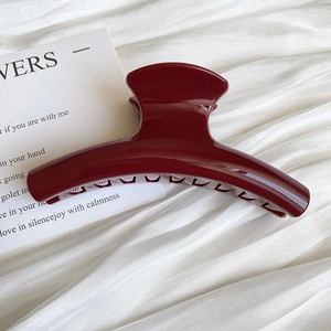Macro view of a large wine red hair claw clip with a glossy finish on white silk