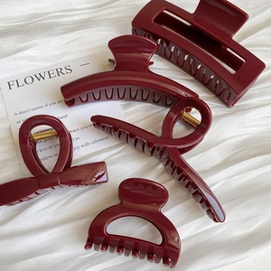 Set of four glossy wine red hair claws in various shapes on a white fabric background