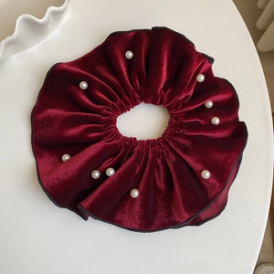 Macro detail of wine red velvet scrunchie decorated with elegant white pearls on a plate