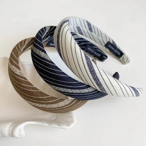 Detail of three striped fabric headbands in brown, navy and beige on a ceramic plate