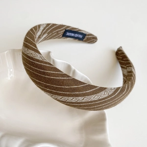Detailed close-up of brown striped fabric headband with Hand Made label on shell tray