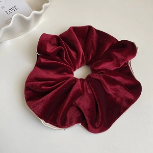 Détail d'un chouchou en velours bordeaux avec bordure dorée et texture plissée chic