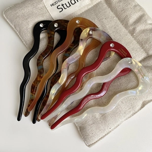 Detail of wave-shaped acetate U-pins in tortoiseshell and pearl colors with small rhinestones
