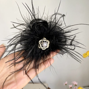Macro detail of black feather hair claw clip featuring a golden flower and grey pearl accent