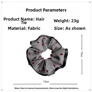 Detail view of a 13cm grey fabric scrunchie with red hearts and black silk edge