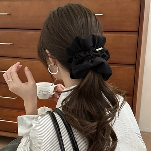 Detail of a large black pleated satin scrunchie with a gold tag on a ponytail