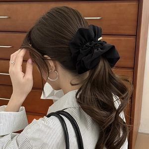 Detail of a large black matte fabric scrunchie with a gold metal tag on a low ponytail