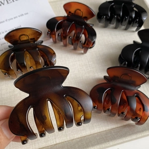 Detail of tortoise shell and black matte hair claws on a tray with a hand holding one