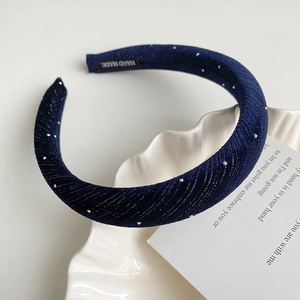 Détail d'un serre-tête bleu marine orné de strass avec étiquette fait main sur plateau