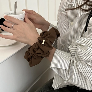 Retro brown oversized scrunchie with metallic label worn on wrist in lifestyle setting