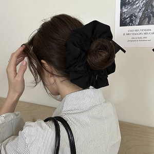 Detail of a large black pleated scrunchie hair tie worn on a messy bun hairstyle