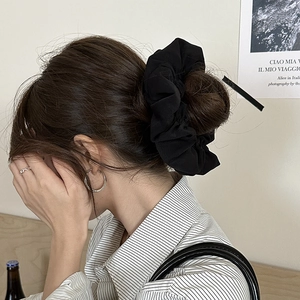 Detail of a large pleated black scrunchie and hair stick set on a female model