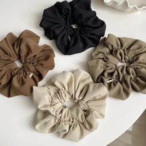 Detail of four chiffon scrunchies in earth tones featuring elegant gold metal buckles