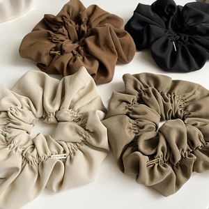 Close-up of pleated scrunchies in earth tones featuring gold Handmade metal labels