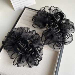 Detail view of black lace polka dot bow hair claws with metal accent in a display box