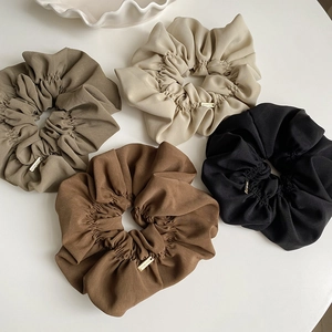 Close-up of four pleated scrunchies in earth tones with elegant gold metal logo tags
