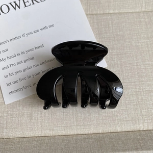 Detail of glossy black claw clip with multi-tooth design on soft beige fabric