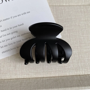 Detail of matte black octopus hair claw clip on beige linen surface with card