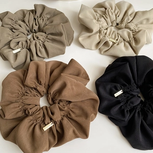 Close-up of four oversized scrunchies in earth tones with gold handmade metal tags