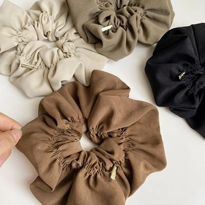 Detail view of elastic scrunchie set in earth tones with refined gold metal labels