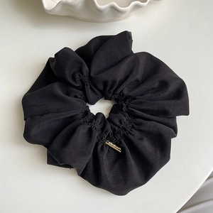 Detailed close-up of a large black pleated fabric hair tie with a gold handmade label tag