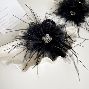 Detail of a black feather hair claw clip with mesh layers and rhinestone floral center