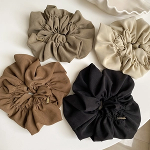 Close-up of four pleated oversized scrunchies in earth tones with gold handmade tags