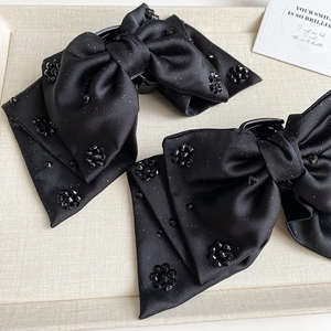 Detail of black satin bow hair claw clip with rhinestones on a beige textured tray