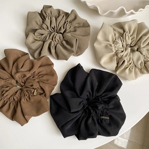 Detail view of retro pleated scrunchies in earth tones with gold handmade metal labels