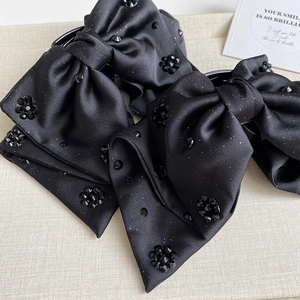 Detail of black satin bow hair clip with sparkling gemstone beads on a textured surface