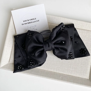 Close-up of black satin bow hair clip with sparkling crystals on a fabric display tray