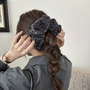 Winter fluffy leopard print scrunchie in dark grey, worn on a braided ponytail style