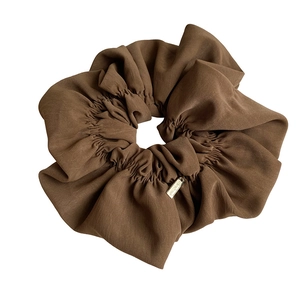 Deep brown pleated scrunchie with elegant golden metal tag on plain white background