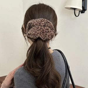 Close-up of a leopard print plush scrunchie worn by a model in a cozy indoor setting