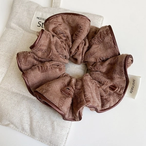 Detailed close-up of a vintage brown fabric scrunchie with handmade tag and satin piping