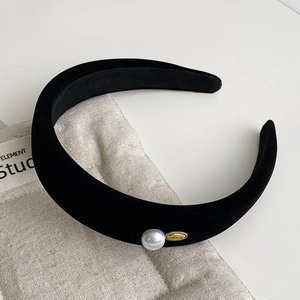 Detailed close-up of a black velvet headband with a single white pearl and gold metal accent