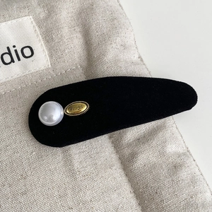 Close-up of black velvet headband featuring a white pearl and golden Wings metal plate