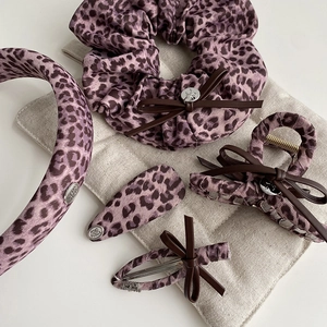 Detail view of purple leopard hair accessories set with brown bows and metal logo charms