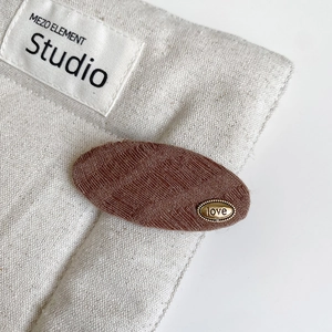Close-up of brown textured fabric hair clip featuring a vintage gold metal Love engraving
