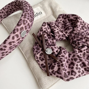 Purple leopard print hair set with plush headband and scrunchie on beige linen
