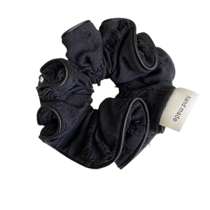 Vintage black fabric scrunchie with frayed edges and a handmade woven label detail