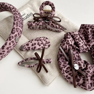 Detail of purple leopard print hair accessory set with leather bow and metal logo charm