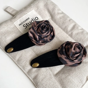 Pair of black flocked hair clips with brown leopard print fabric roses and gold logo