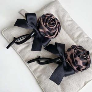 Detailed view of leopard print rose hair clips with black satin bows on fabric background