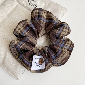 Detailed close-up of brown and blue plaid scrunchie fabric with a bear woven label