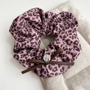 Close-up of purple leopard print scrunchie with brown leather bow and silver metal buckle
